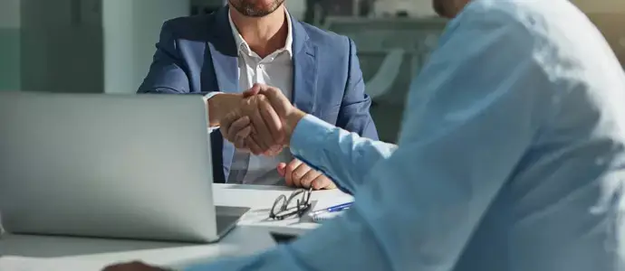 Two professionals shaking hands over a desk